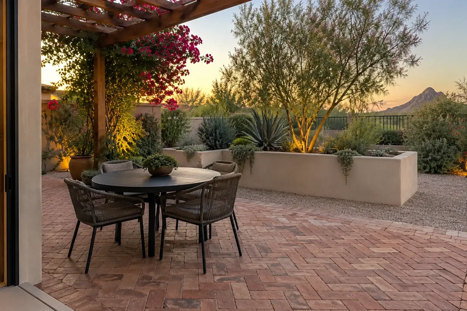 Brick paved dining patio under a pergola with bougainvillea, a round table and desert planting at sunset
